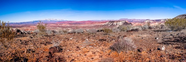A panorama of painted desert hills in pinks and reds under a deep blue sky, snow-capped mountains on the horizon.