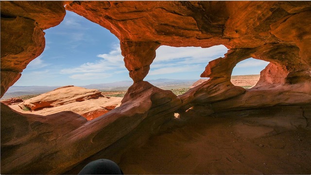 Looking out from inside a red rock alcove through natural stone windows to the desert beyond.