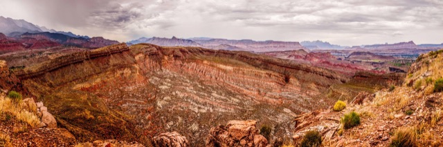A sweeping panorama of layered red rock canyons and distant cliffs under storm clouds.