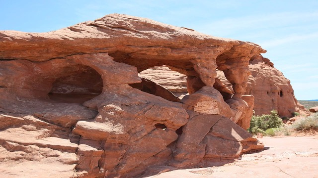 A weathered red sandstone formation full of natural windows and small arches under a clear sky.